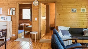 Een houten blokhut van binnen met een bank, stoelen, een eethoek en een keuken.