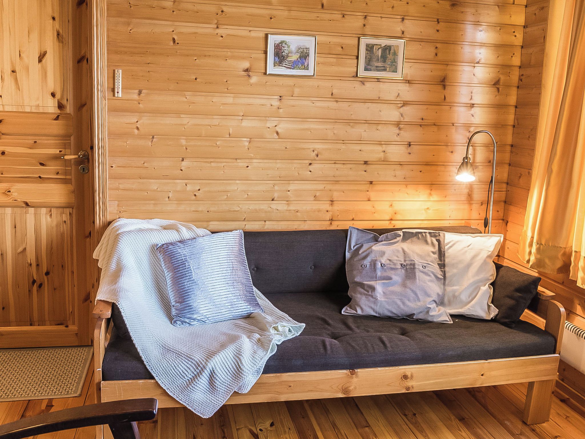 Puinen mökki, jonka sisustuksessa on sohva, tyynyjä, lamppu ja seinällä olevia kehystettyjä kuvia.