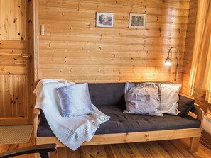 L’intérieur d’un chalet en bois, avec un canapé, des coussins, une lampe et des tableaux encadrés accrochés au mur.