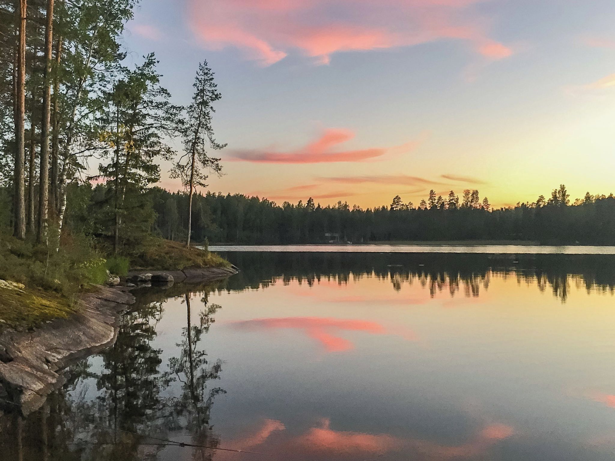 Tyyni järvi, jonka pinnassa heijastuvat puut ja taivas on kirkas.