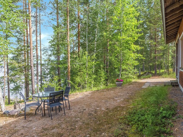 A forested area with a table and chairs, a pathway, and a building.