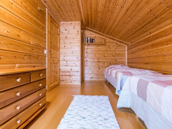 Acogedora habitación tipo cabaña de madera con una cama litera, una pequeña estantería y una alfombra tejida en el suelo.