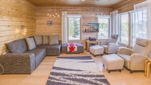 A cozy log cabin interior with a sofa, chairs, a rug, and a TV on a wooden shelf.