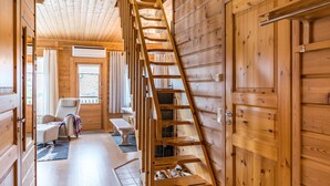 A wooden cabin interior with a wooden staircase, a chair, a bench, and a door.