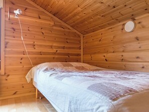 A wooden cabin room with a bed, a circular window, and a wall-mounted light fixture.