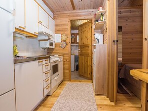 A compact kitchen with white cabinets, a microwave, and a stove. A wooden door leads to a bedroom with a bed. - Piilola nr 2 by Interhome (Kuusamo)