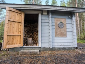 Une petite cabane en bois, dont la porte est ouverte, laissant apercevoir une pile de bois à l’intérieur.