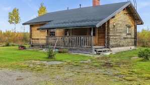 Puuinen mökki, jossa on kuisti, savupiippu ja sorapäällysteinen ajotie.