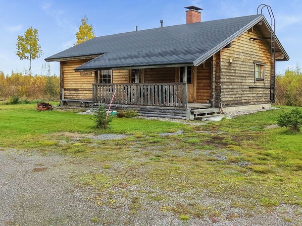 A wooden cabin with a porch, a chimney, and a gravel driveway.