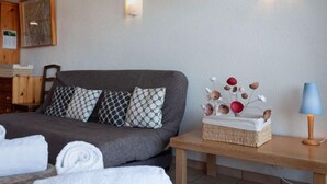 Ein ordentlich bezogenes Bett mit gemusterten Kissen, ein Nachttisch mit Lampe und eine dekorative Vase mit getrockneten Blumen.