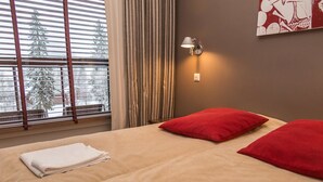 Ein Hotelzimmer mit einem großen Bett, zwei roten Kissen, einem weißen Handtuch, einem Fenster mit Jalousien und einer Wandlampe.