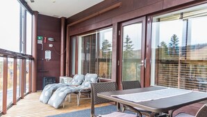 Ein überdachter Außenbereich mit Tisch, Stühlen, großen Fenstern und einer Holzterrasse.