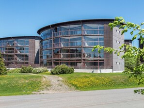 Un bâtiment moderne à la façade incurvée en verre, entouré d’une pelouse bien entretenue et d’un chemin de gravier menant à l’entrée.
