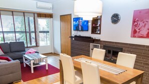 Ein modernes Wohnzimmer mit Kamin, einem Esstisch mit Stühlen, einer Couch, einem Fernseher und einer Wanduhr.