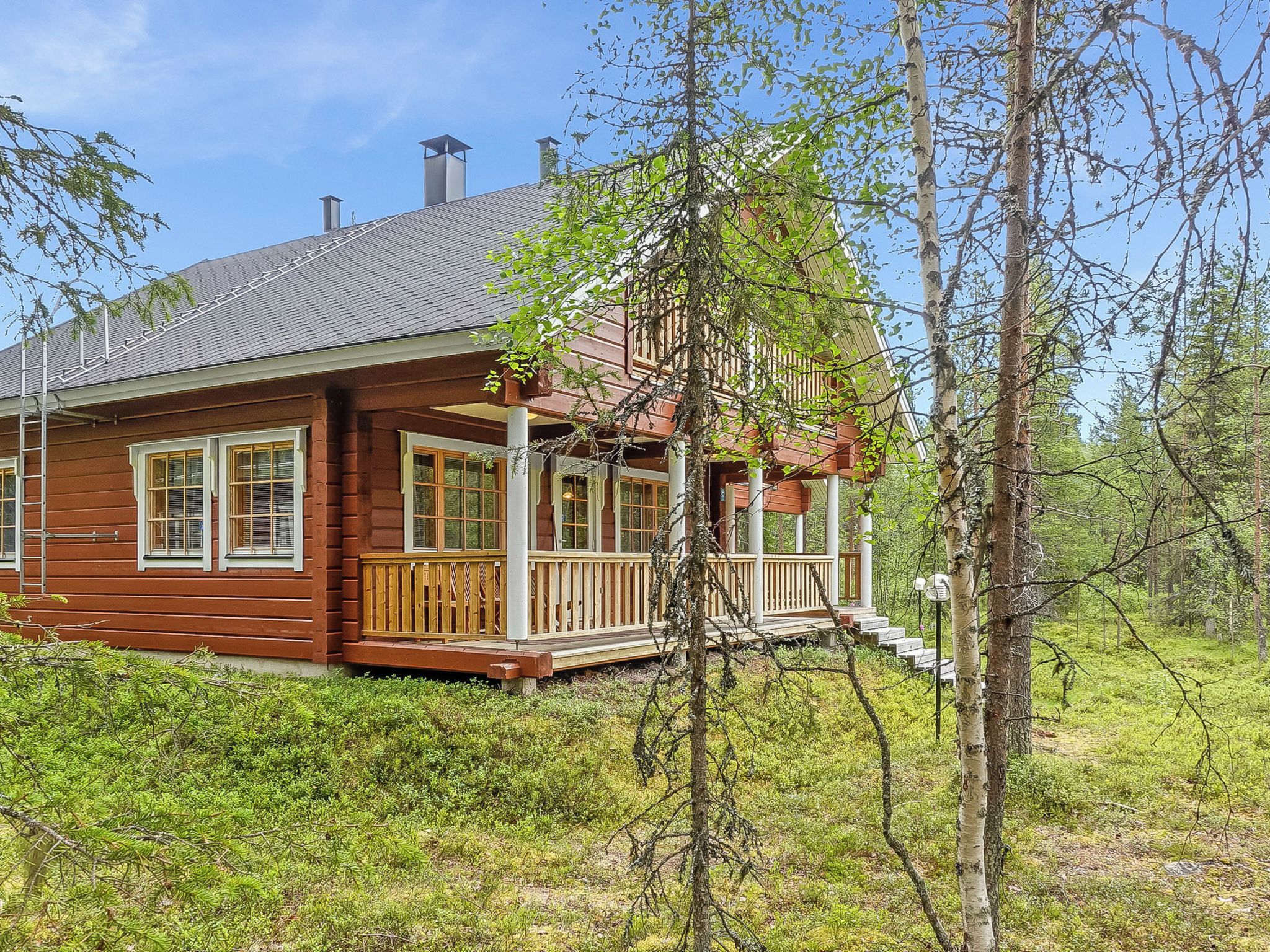 A wooden cabin with a porch, surrounded by trees and greenery.