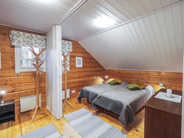 A cozy attic bedroom with a sloped ceiling, wooden walls, a bed with grey bedding, and a radiator.