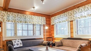 Una habitación acogedora con dos sofás, una mesita de centro y una silla. Hay ventanas con persianas y una lámpara de techo.