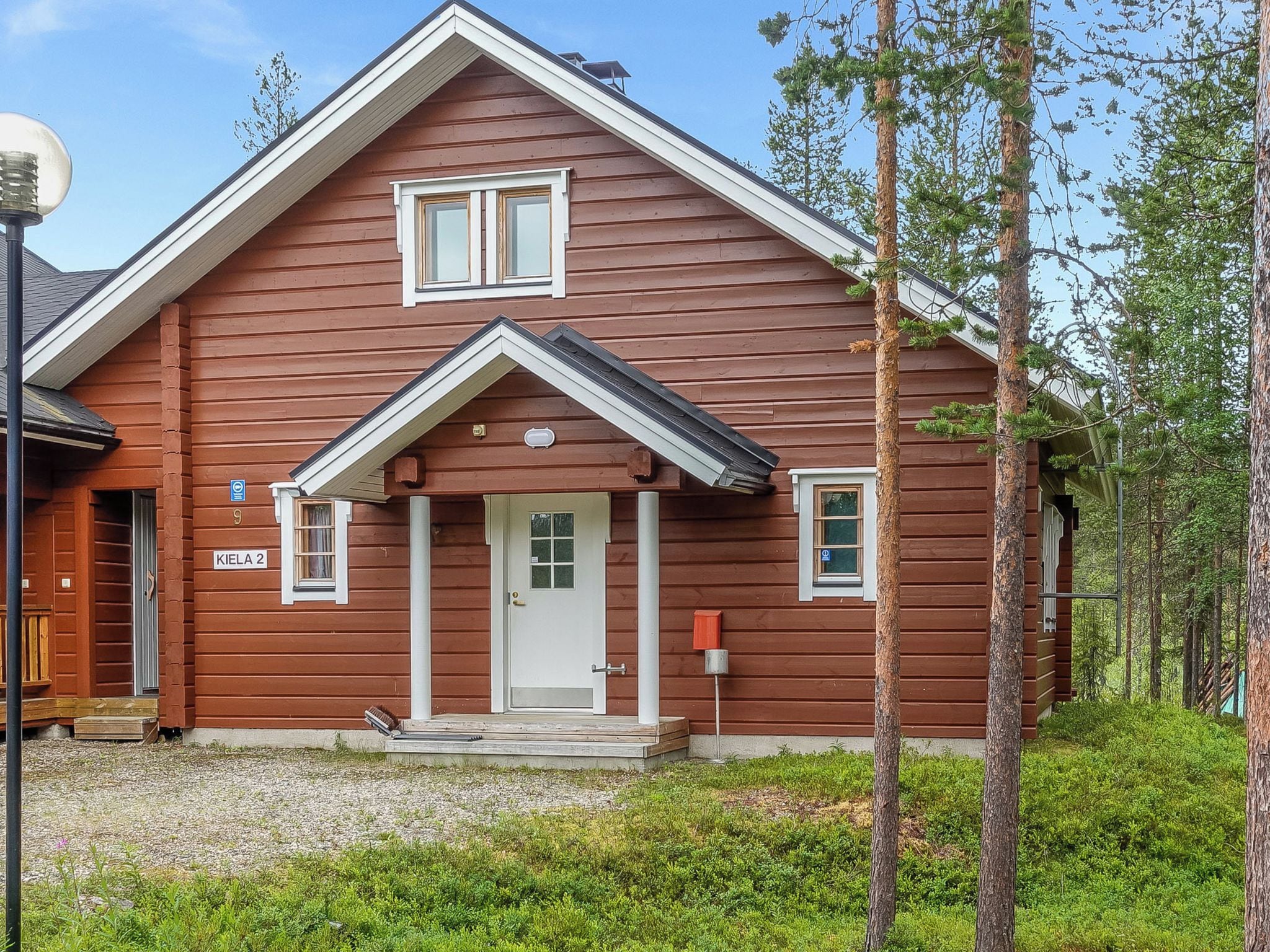 A two-story wooden cabin with a front porch, a mailbox, and a door with a number plate.