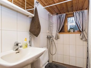 A bathroom with a sink, shower, and window with curtains.