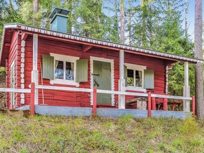 Une cabane rouge avec un porche, deux fenêtres avec des volets et une cheminée.