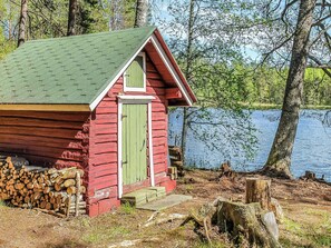 A small cabin with a green door and a red exterior, situated by a lake surrounded by trees. - Heinälampi by Interhome (Parikkala)