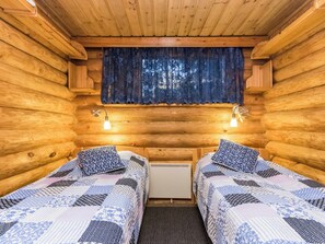 A cabin with two beds, each with a patterned bedspread, a window with a blue curtain, and two wall-mounted lights. - Heinälampi by Interhome (Parikkala)