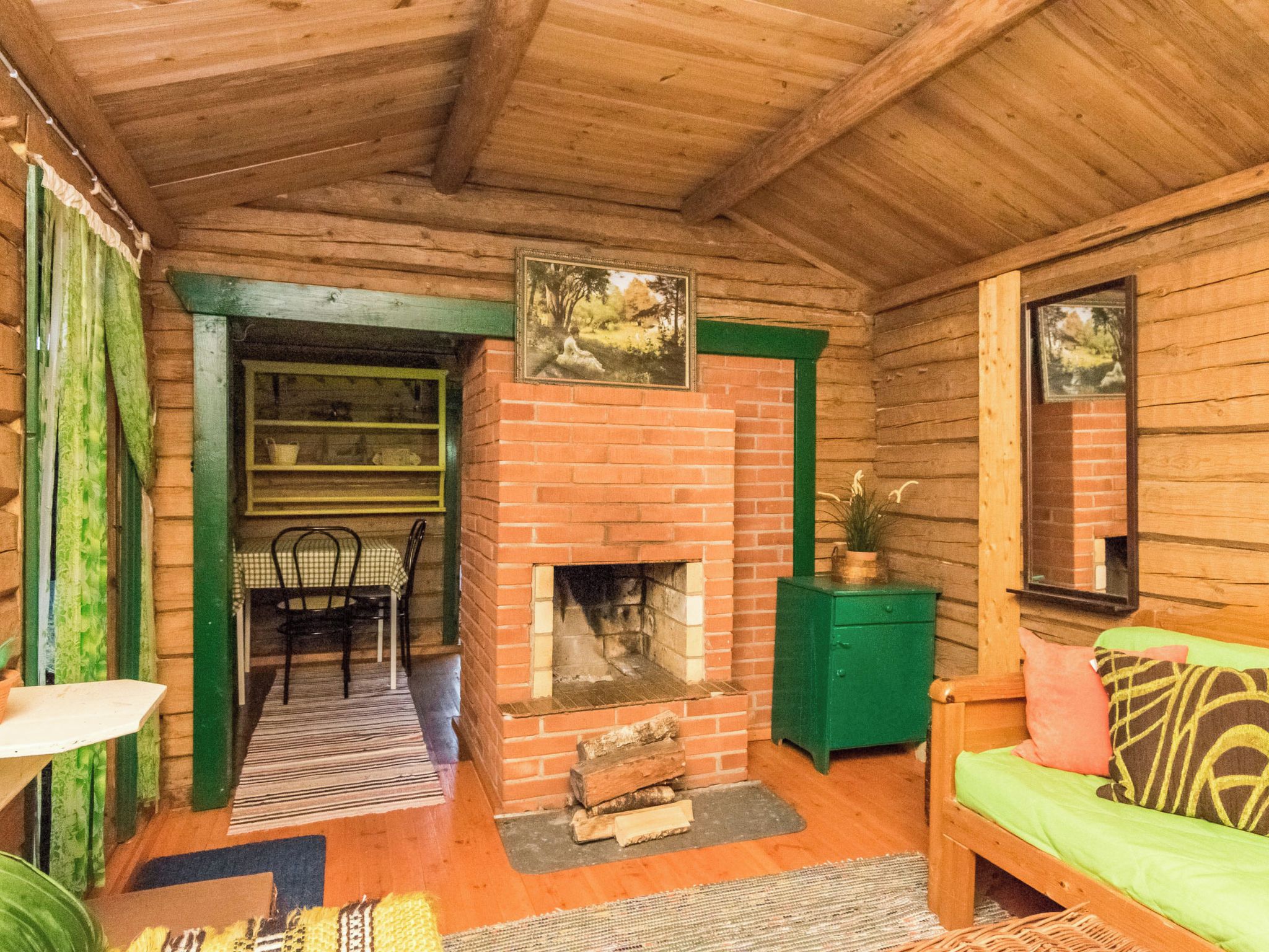 Habitació acollidora amb una llar de foc de maó, un armari verd, una banca de fusta i una zona de menjador amb una cadira i taula.