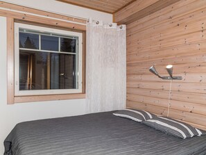 Una habitación con cama, ventana con cortinas y una lámpara fijada a la pared.