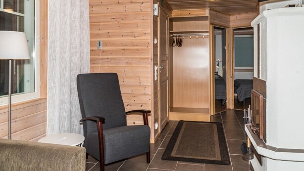 Un interior de madera con una silla, una mesita, un televisor y una puerta que da a otra habitación.