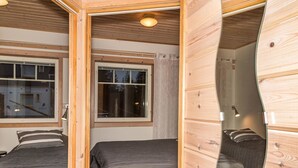 Habitación pequeña con dos camas, una ventana y paredes de madera.