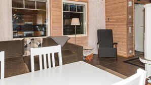 Una habitación acogedora con paredes de madera, una mesa blanca, sillas marrones y blancas, una lámpara y un sillón con cesta de almacenamiento.