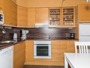 Une cuisine compacte dotée de meubles en bois, d’un four encastré, d’une machine à café et d’un réfrigérateur.