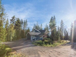 Een huis met een grindpad, omgeven door hoge bomen en een heldere lucht.