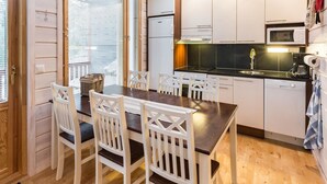 Cocina compacta con armarios blancos, encimera oscura y comedor con sillas blancas.