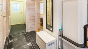 Un pasillo estrecho con una puerta de madera que da a una habitación, un lavamanos blanco con un espejo y una herramienta de limpieza azul en la pared.