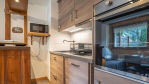 Moderni keittiö, jossa on puiset kaapit, sisäänrakennettu mikroaaltouuni ja suuri ikkuna, josta avautuu näkymä puutarhaan.