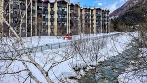A multi-story building with balconies, a river in the foreground, and a mountainous backdrop. - Grand Roc by Interhome (Argentière)