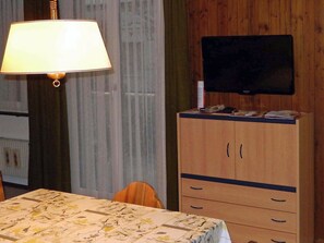 Una habitación con una cama, un televisor montado en un mueble de madera y una mesa con mantel estampado.