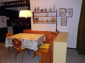 Un comedor con una mesa preparada para cuatro personas, un banco y una cocina al fondo.