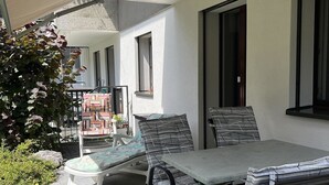 Ein Terrassenbereich im Freien mit Tisch und Stühlen, ein überdachter Sitzbereich und Blick auf die Außenansicht des Gebäudes.