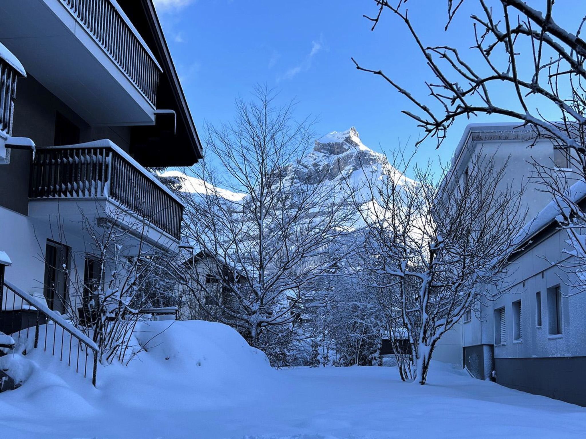 Une rue enneigée, avec des bâtiments et une montagne en arrière-plan.