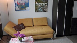 Ein Zimmer mit einer Couch, einem kleinen Tisch mit Blumen in einer Vase und zwei Bildern an der Wand.