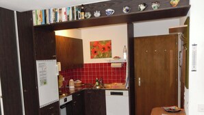 Eine kleine Küche mit Kühlschrank, Backofen und Geschirrspüler, einer roten Fliesenwand und einem kleinen Regal mit Dekoration.