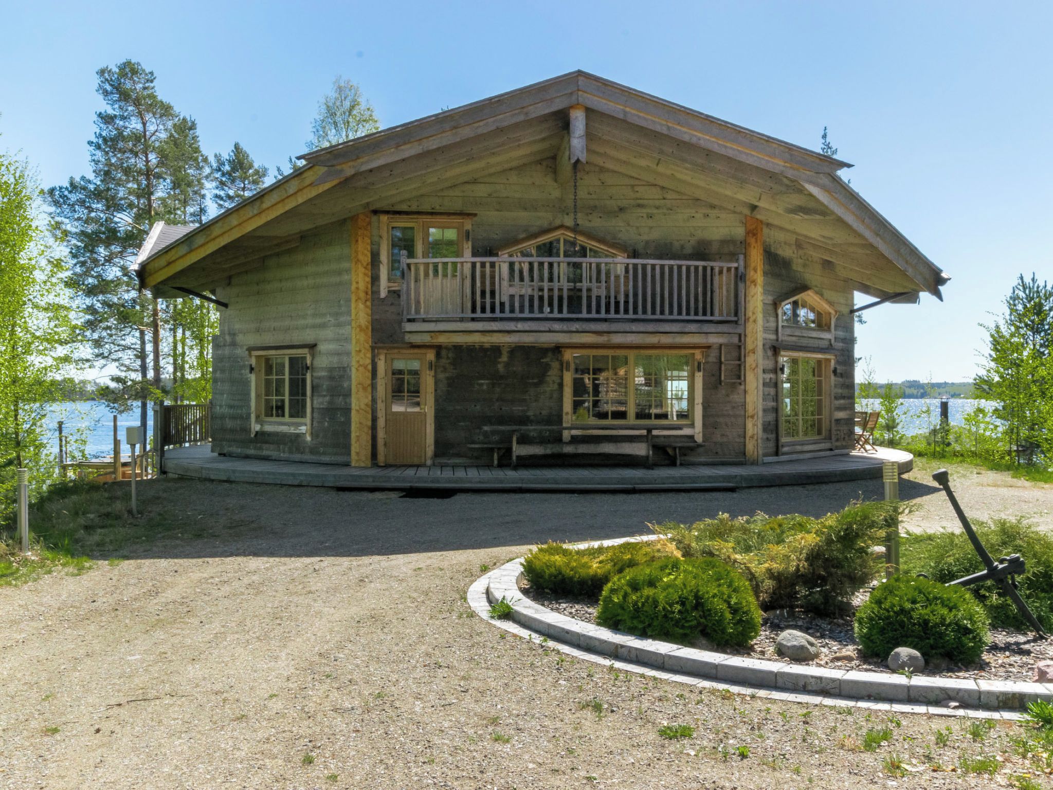 Une cabane en rondins à deux étages, dotée d’un balcon, située au bord d’un lac.