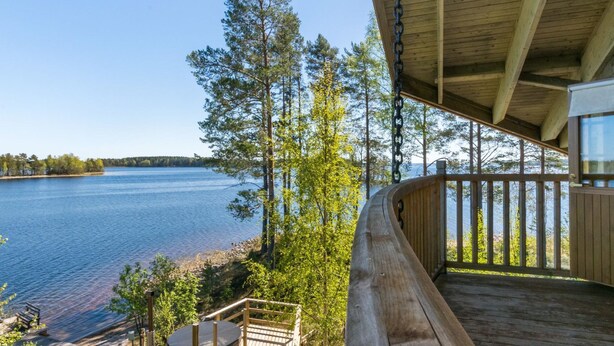 A wooden deck with a hot tub and seating area overlooking a lake, surrounded by trees. - Villa pyöriäinen by Interhome (Kerimäki)