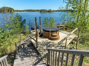 Eine Holzterrasse mit Whirlpool und Sitzbereich mit Blick auf einen See.