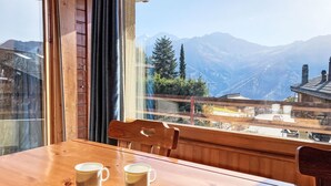 A wooden table with two white mugs, a window with a view of mountains, and a wooden railing. - Mogador 13 by Interhome (Verbier)