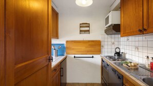 A compact kitchen with wooden cabinets, a microwave, a kettle, and a tiled backsplash. - Mogador 13 by Interhome (Verbier)