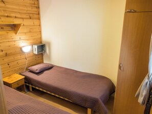 A single bed with a headboard, a bedside table, a lamp, and a wardrobe in a room with wooden walls.