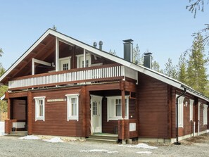 A two-story wooden cabin with a balcony, a chimney, and a sign reading 'Hirvas-Levi Oy 37'.